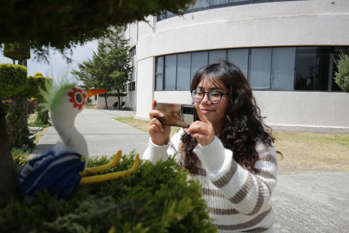 Alumna de la UAEH tomando fotografía a una escultura de una garza