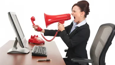 Mujer en traje de oficina gritando a través de un megáfono rojo hacia un teléfono antiguo, representando el acoso por cobranza bancaria.