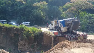 Personas cruzan caminando entre fracturas y tierra reblandecida mientras intentan retirar el tráiler atrapado en Tenango de Doria