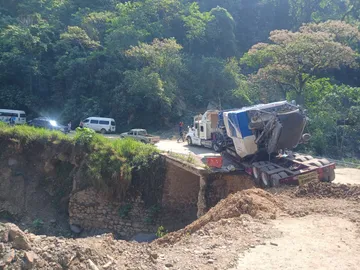 Personas cruzan caminando entre fracturas y tierra reblandecida mientras intentan retirar el tráiler atrapado en Tenango de Doria